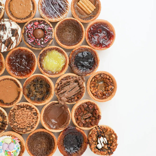 Butter tart halves on a plate with a glossy gooey filling, a dusting of sugar, and a sprinkle of flaky salt