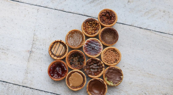 A tray of golden butter tarts with glossy caramel filling cooling on a wire rack, set against a warm, cozy bakery backdrop