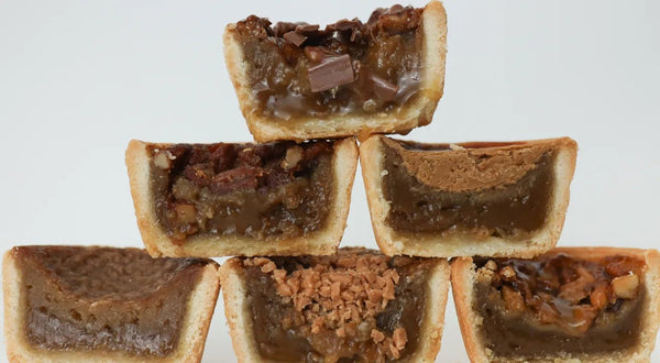 Close-up of a flaky butter tart with a glossy caramel filling on a wooden board, dusted with a pinch of sugar