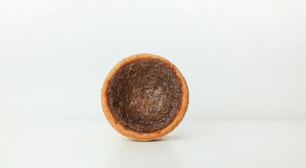Close-up of a flaky butter tart with a glossy, caramel-like filling and a golden crust, set on a light background